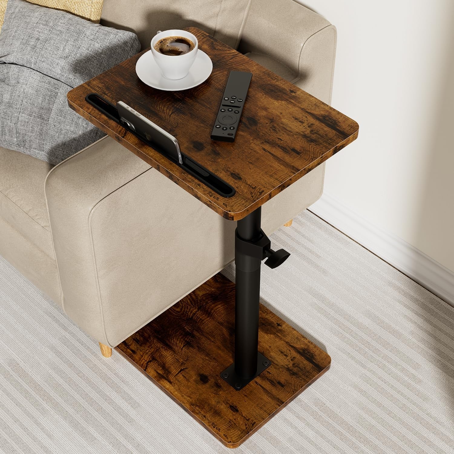 Dark wood side table next to a beige sofa holding a cup, remote, and phone in a slot