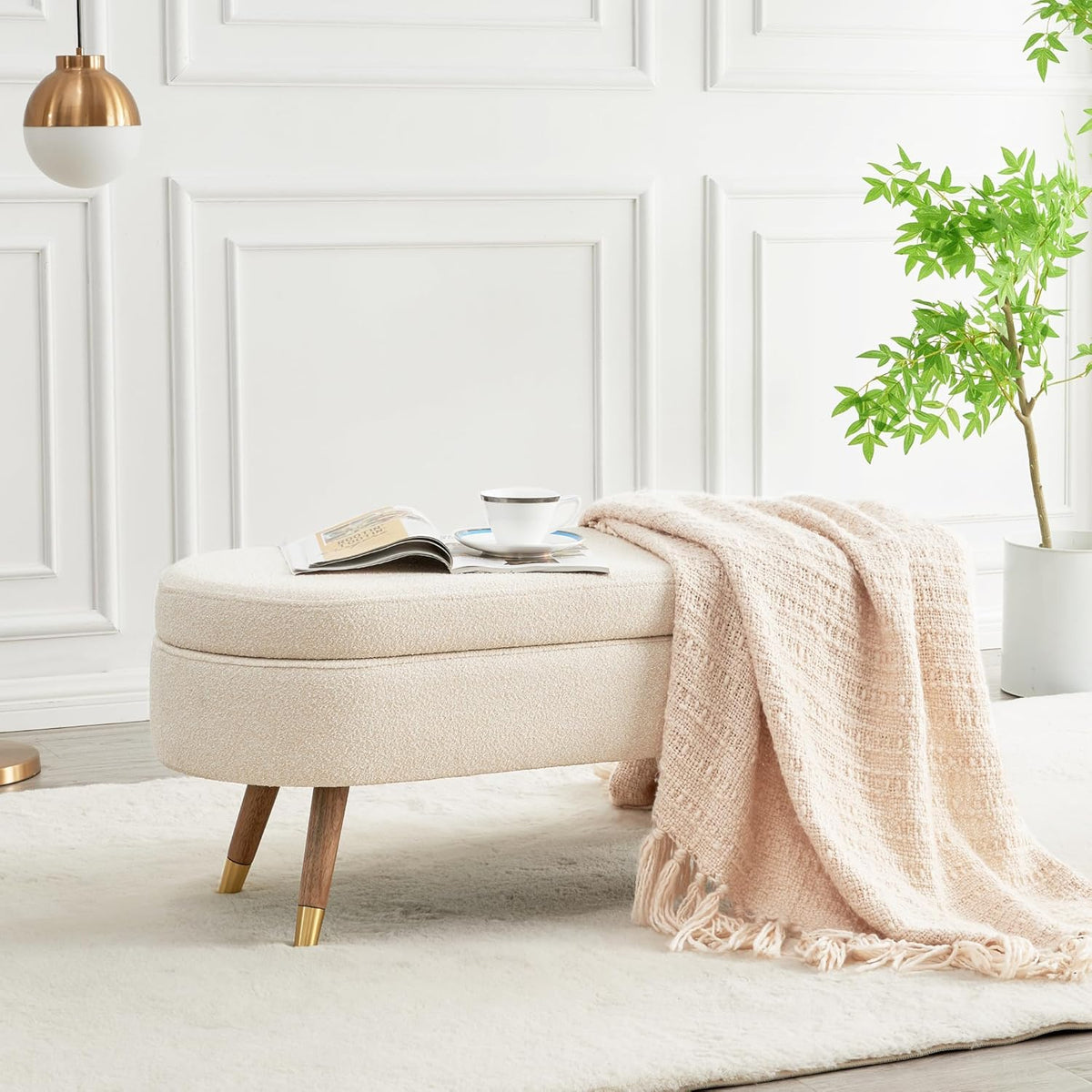 Beige textured fabric storage bench styled at the foot of a bed with a throw blanket and a cup on top