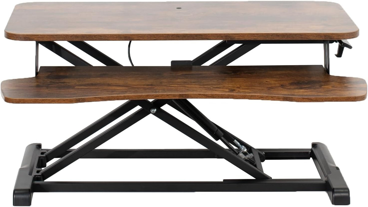 Low front view of a standing desk riser showing keyboard tray and scissor lift mechanism in dark wood