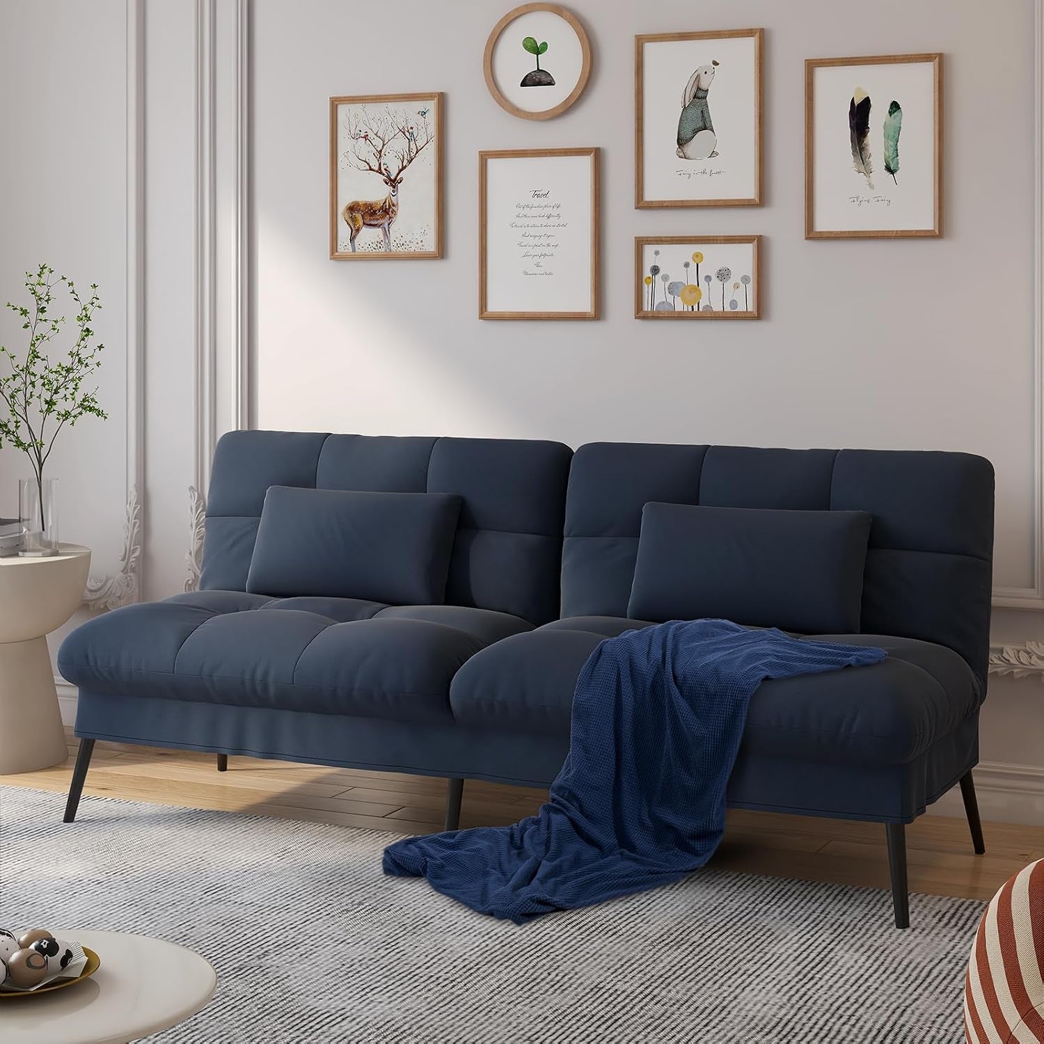 Navy blue futon sofa with tufted cushions and a draped blue throw in a styled living room.