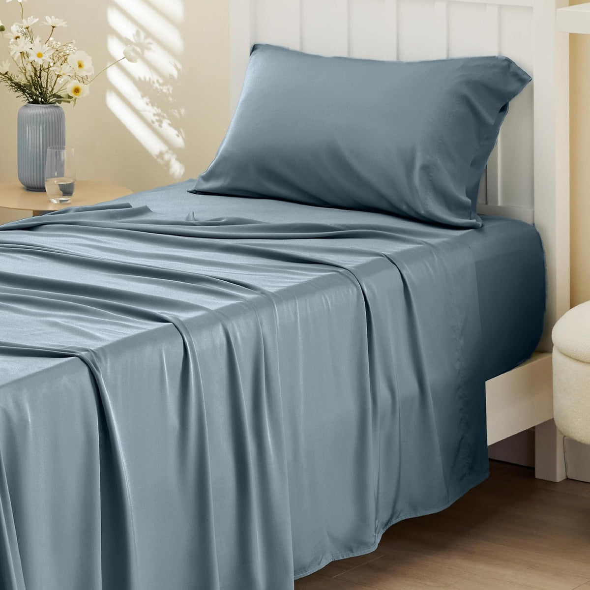 Side-on shot of a bed corner showing smooth deep blue sheets and a single pillow against a white headboard.