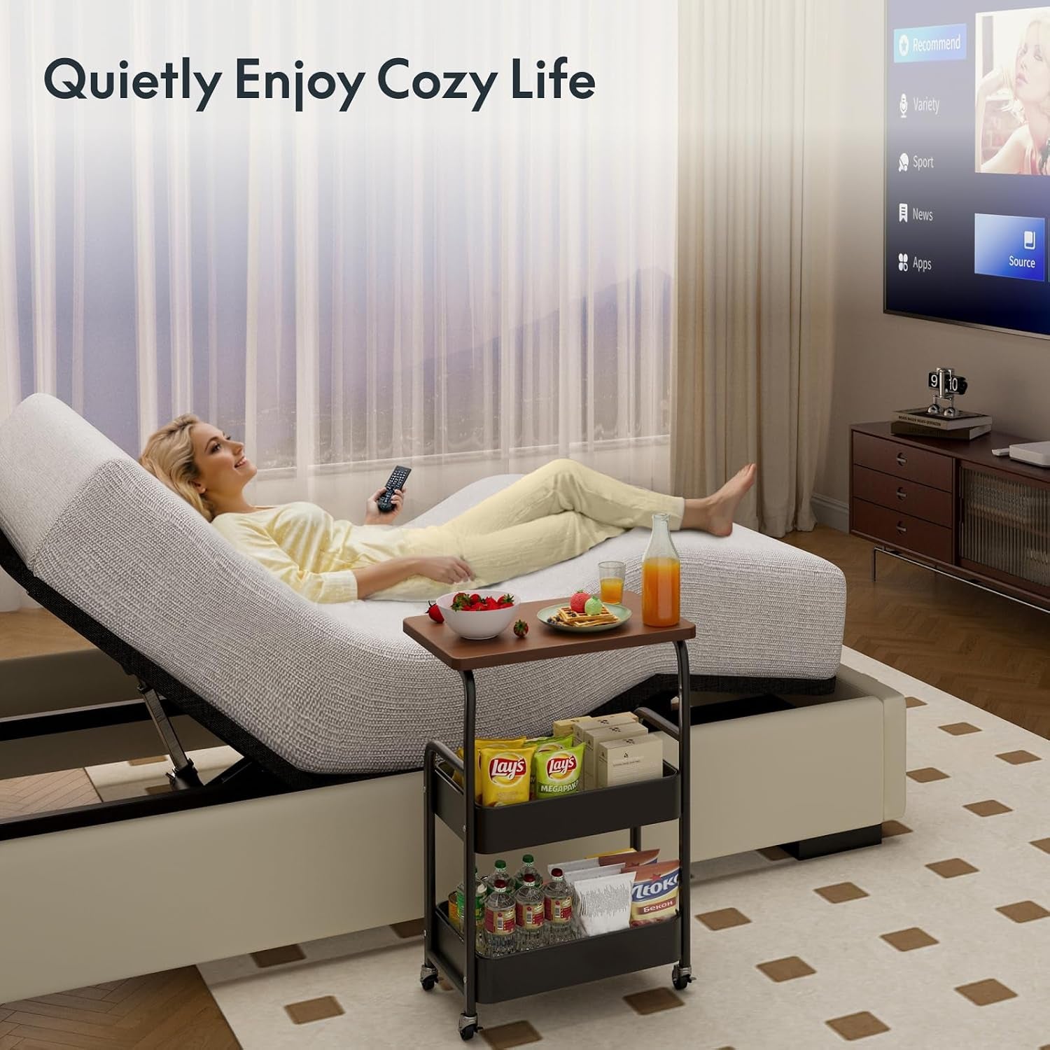 Woman reclining on remote‑controlled base watching TV with a small snack cart beside the bed