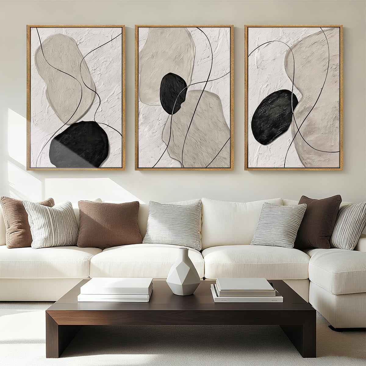 Triptych of neutral abstract paintings with black organic shapes hung above a white sectional sofa in a living room.