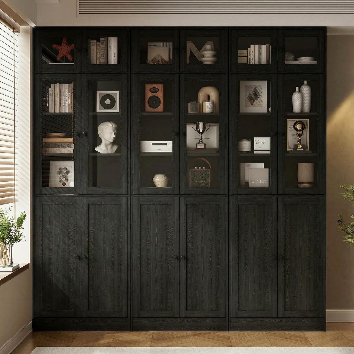 Full wall of tall black bookcases with glass upper doors and closed lower cabinets in a dimly lit room.