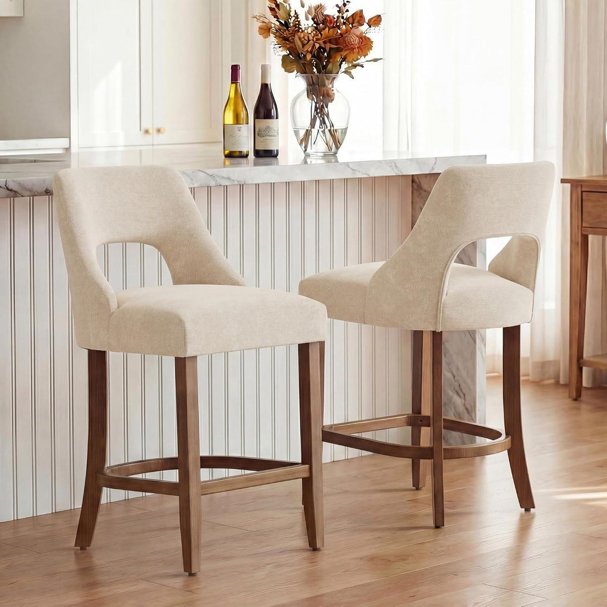 Pair of beige bar stools at an island, angled to show front and back profiles and wood footrests