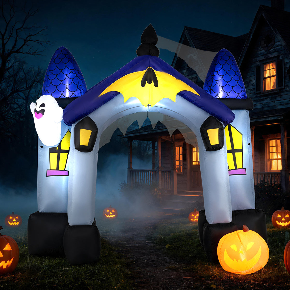 The illuminated inflatable castle arch stands outside a dark house amid fog and glowing jack-o’-lanterns.