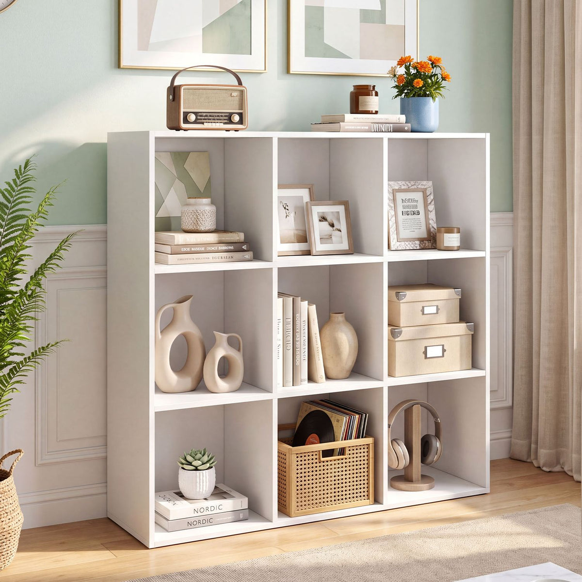 White nine-cube bookcase styled with books, framed photos, baskets and decor in a bright living room.
