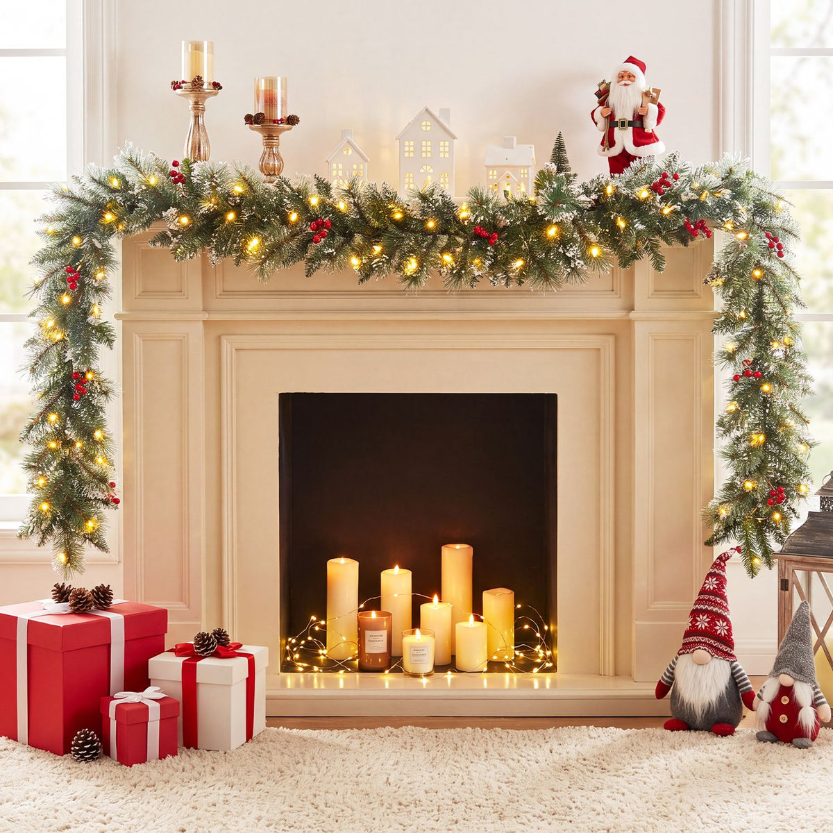 Illuminated greenery drapes across a cream fireplace, with candles, gifts and holiday figures around it.