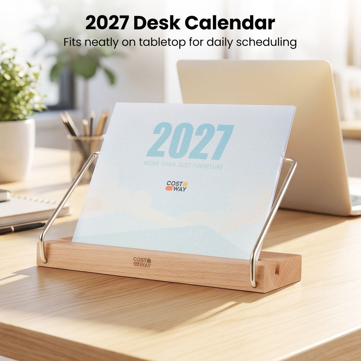 Desk calendar on a wooden stand sits on a sunlit desk beside a laptop and stationery.