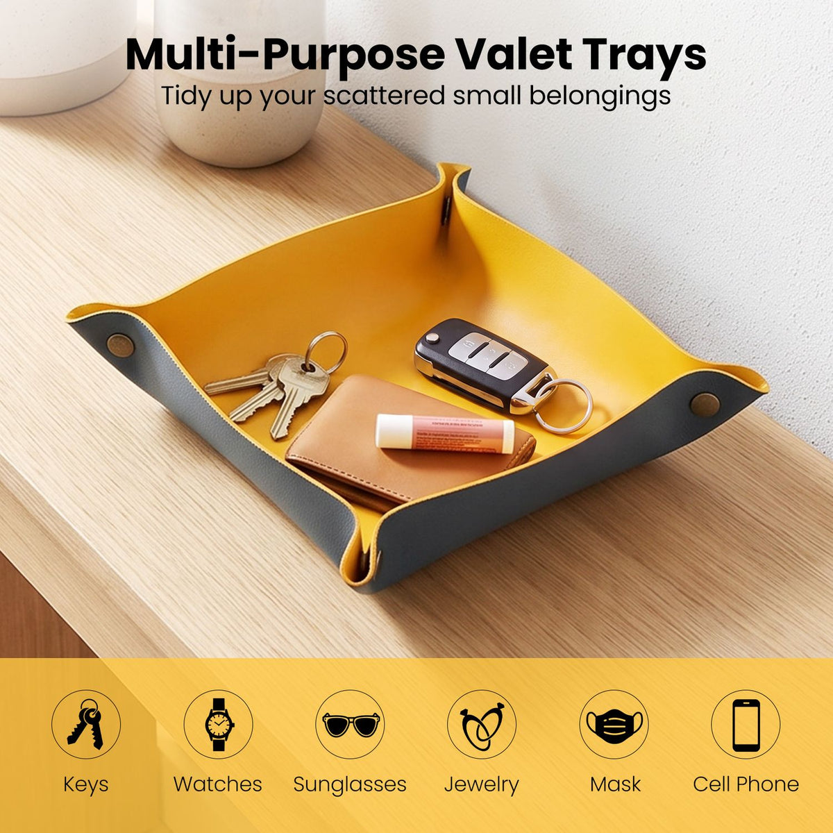 Yellow-and-gray valet tray holding keys, a car remote, a small wallet, and a tube on a wooden table.