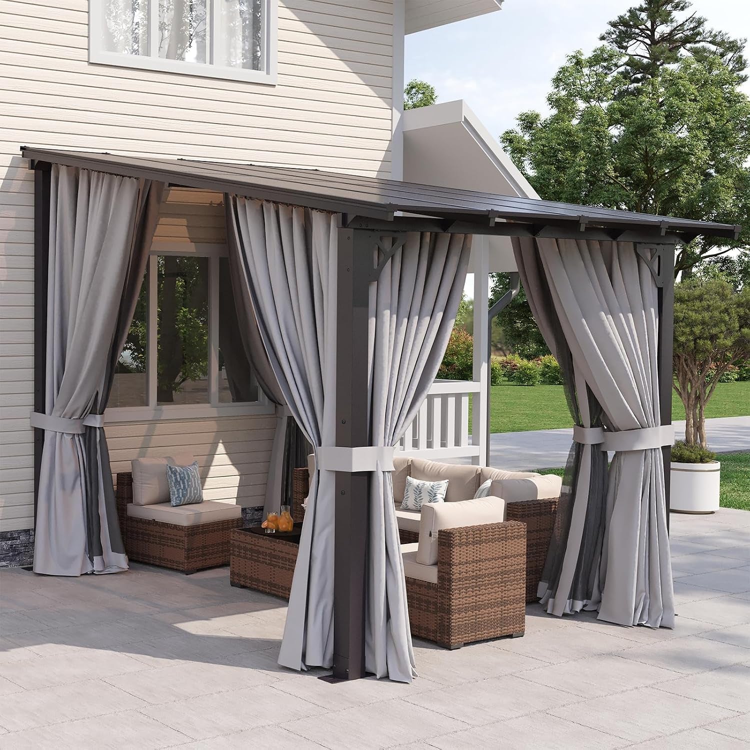 Angled view of the same attached pergola shown with light gray curtains tied to posts above woven seating on a stone patio.