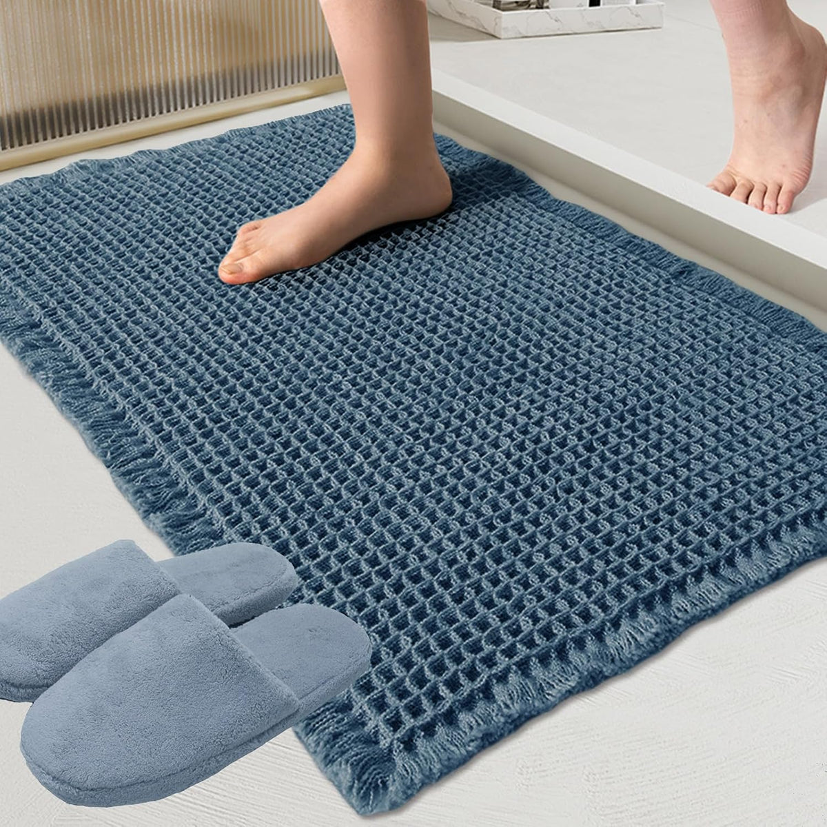 Close-up of a blue waffle-textured bath mat with a bare foot stepping on it and slippers at the corner.