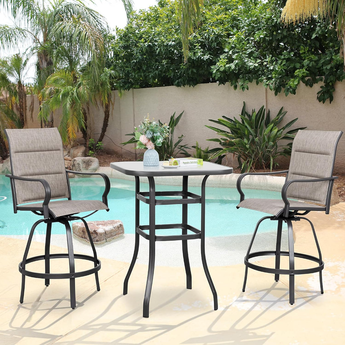 Front view of two taupe sling swivel chairs and square table by the pool with plant-filled background
