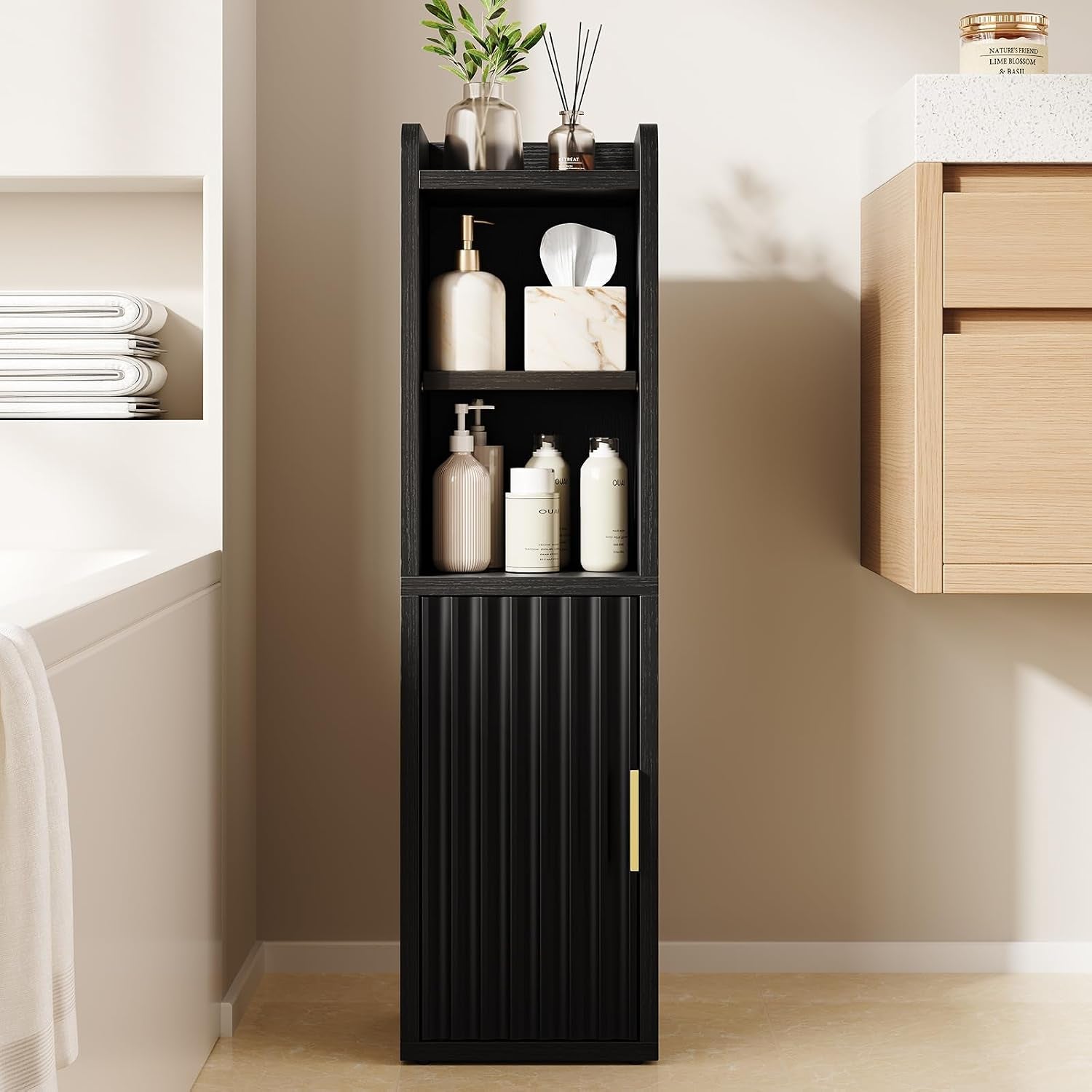 Tall narrow black bathroom storage cabinet with fluted lower door, gold handle, open shelves holding bottles and a plant on