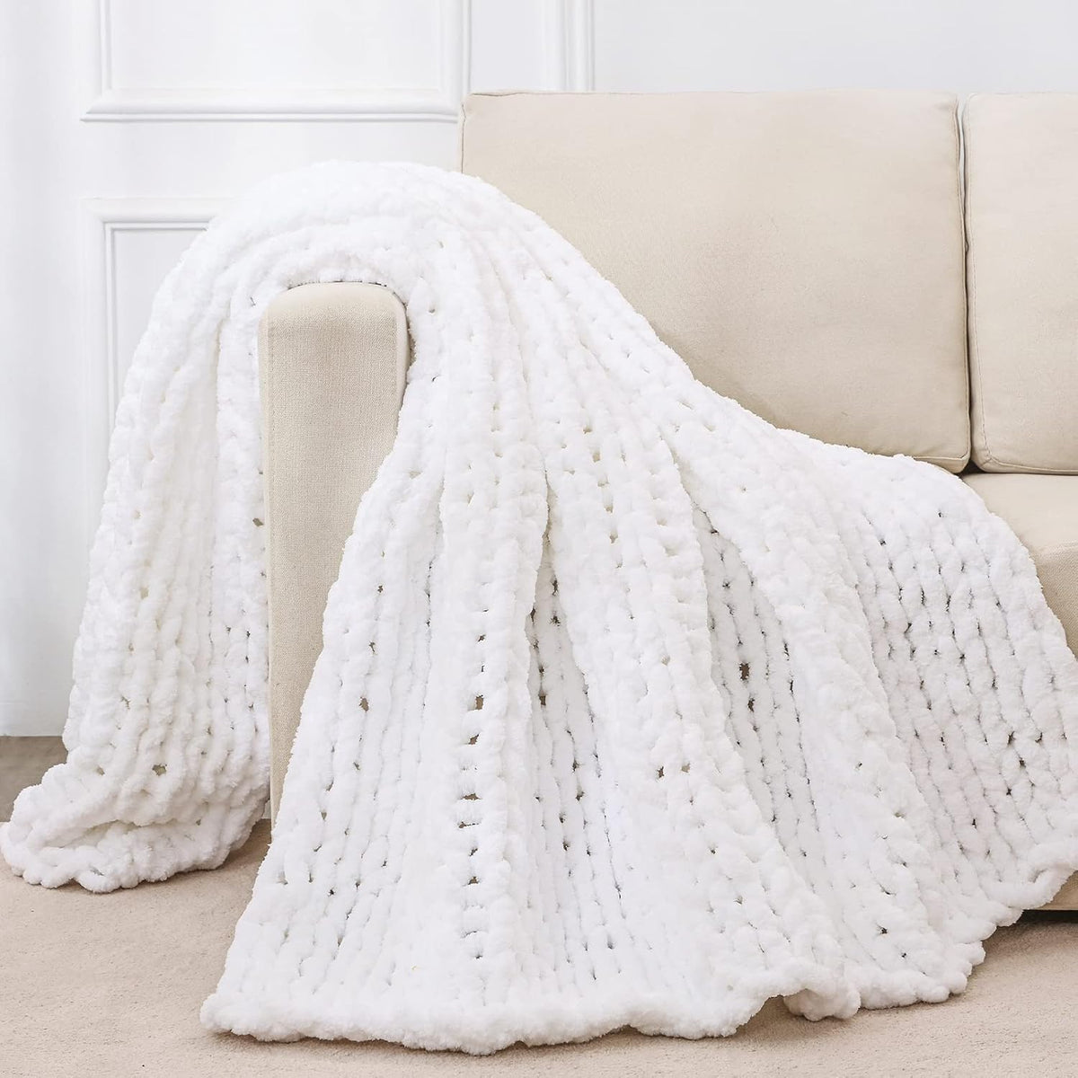 White chunky knit throw casually draped over the arm of a beige sofa, showing looped knit pattern.