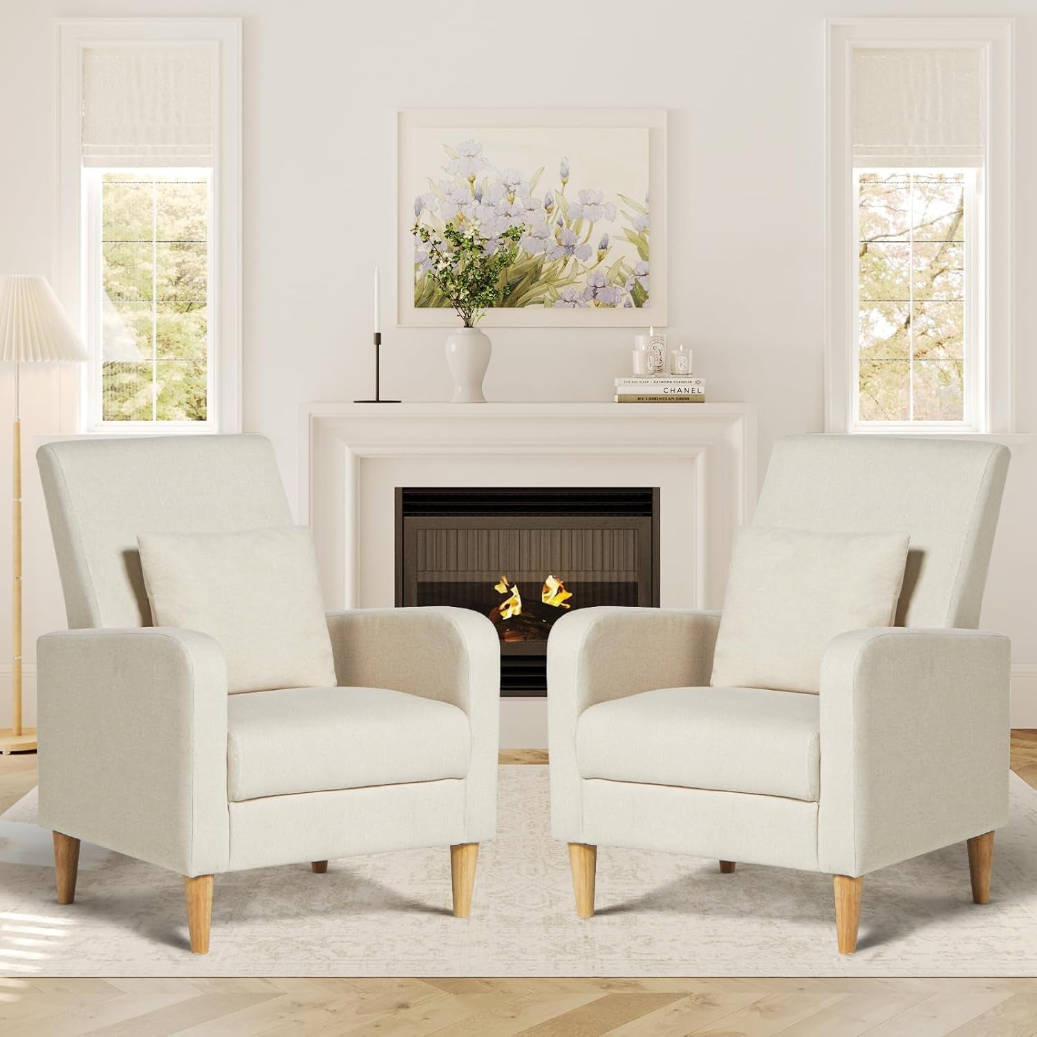 Two cream high-back accent chairs with pillows positioned in front of a fireplace in a bright room.