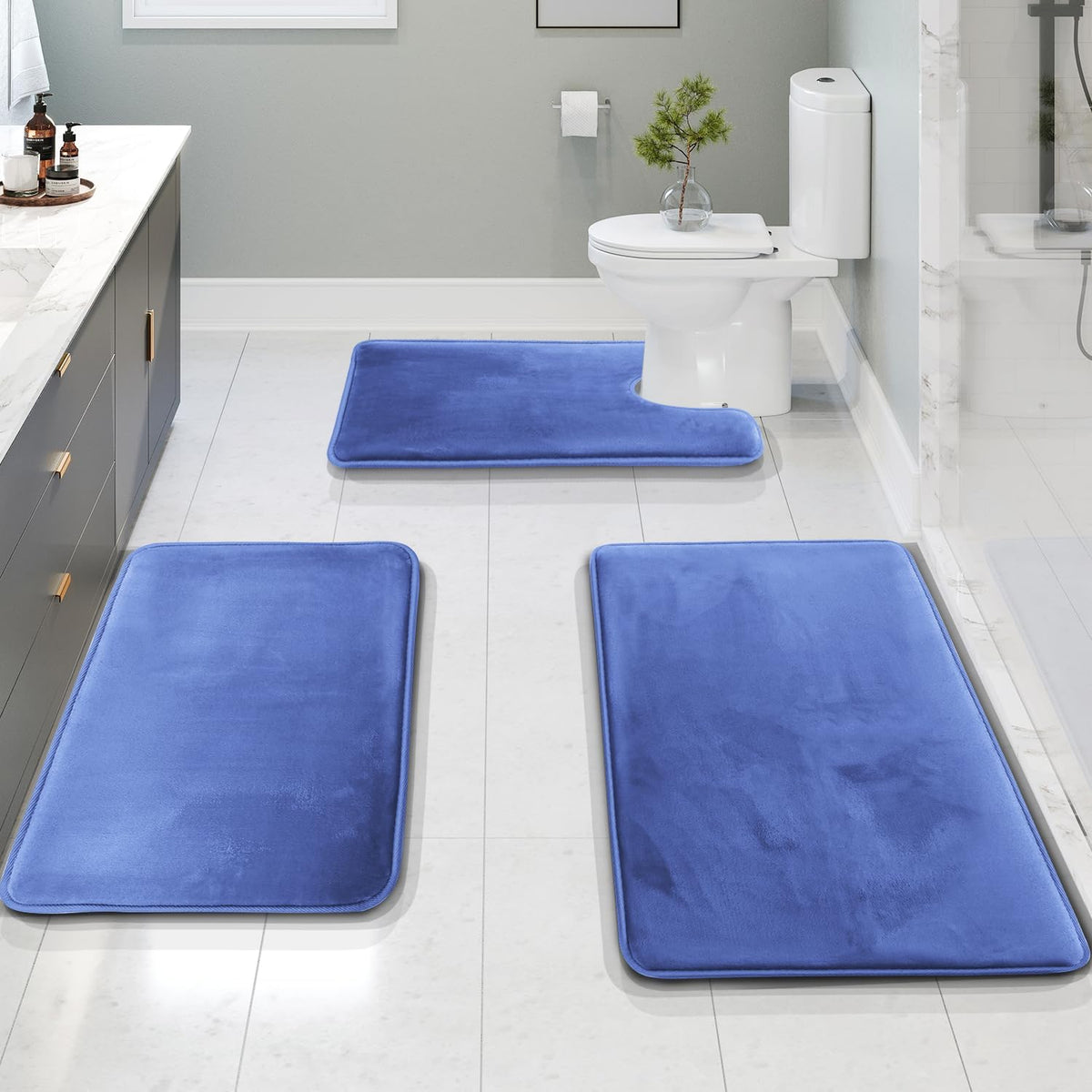 Low-angle view down a tiled bathroom showing two rectangular blue mats in foreground and a U-shaped mat at the toilet