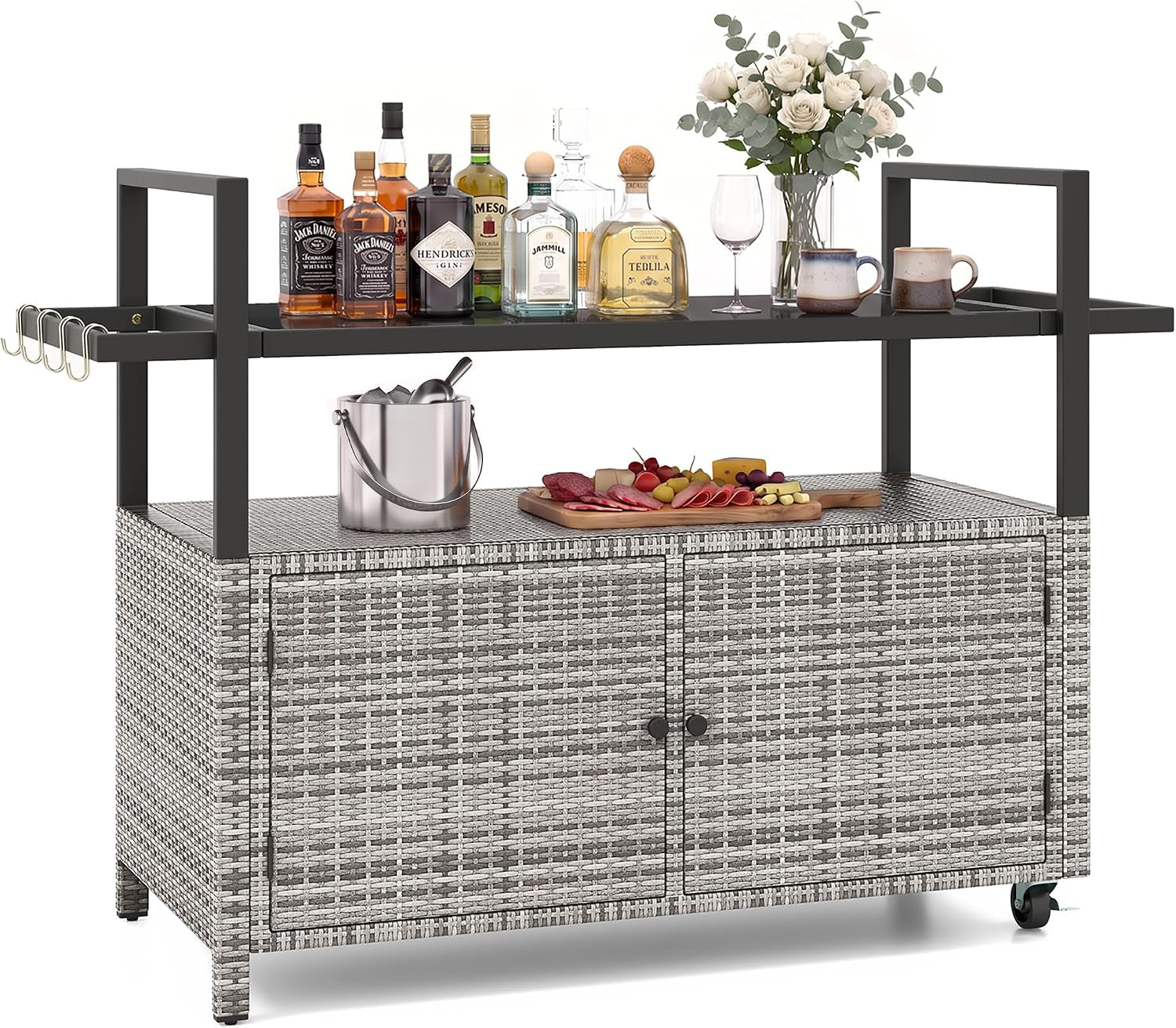 Front view of light-gray woven rattan bar cart with black top rail, bottles and a vase on the glass top, cabinet doors