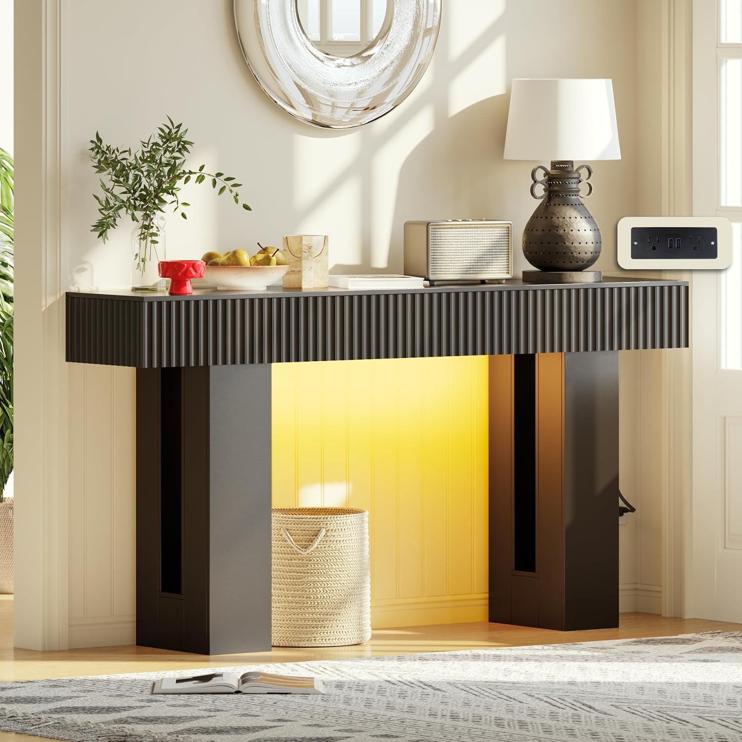 Black-finish console in an entryway with warm backlighting, tabletop decor and a visible wall outlet panel.