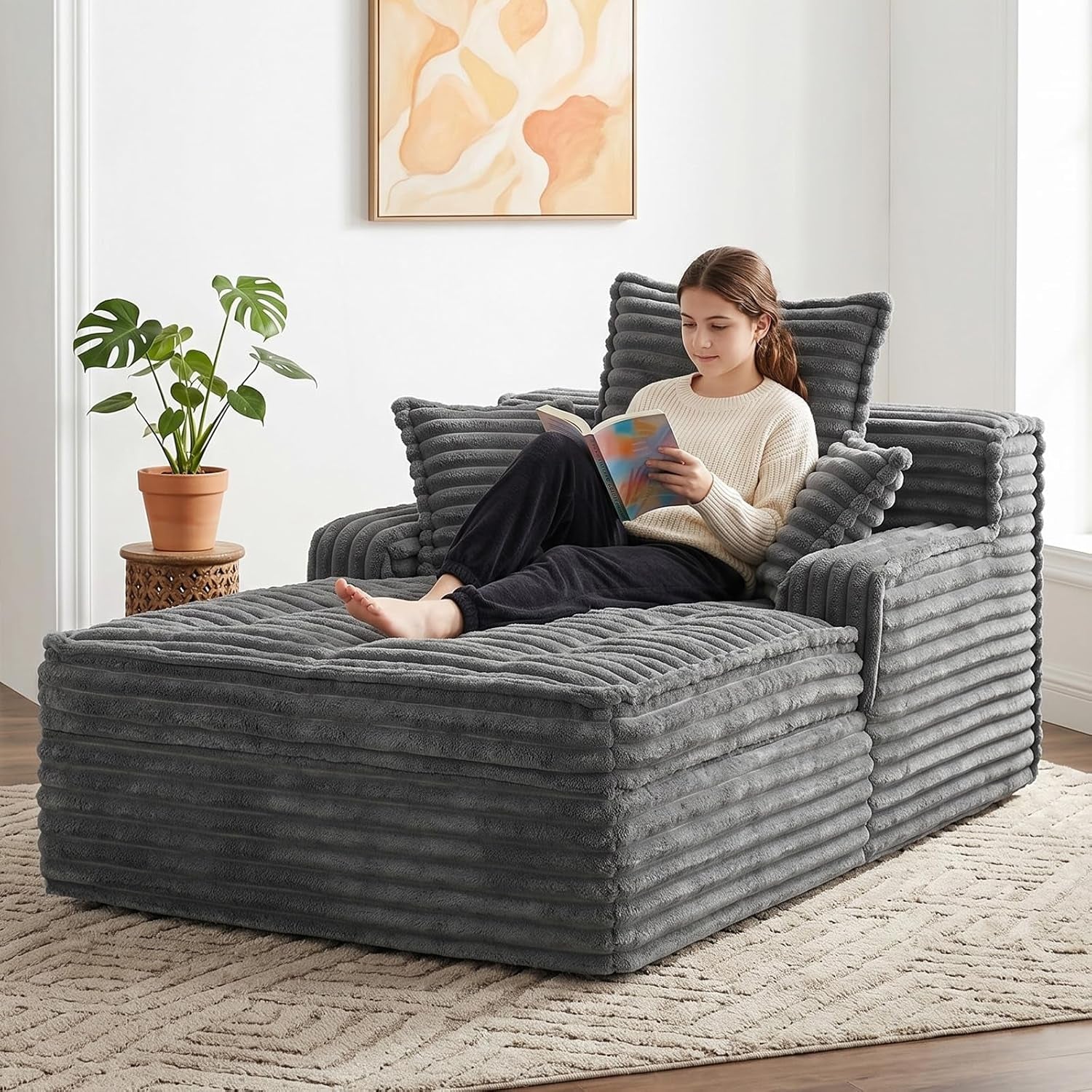 Gray corduroy chaise lounge with ribbed texture and three pillows, woman reading on it