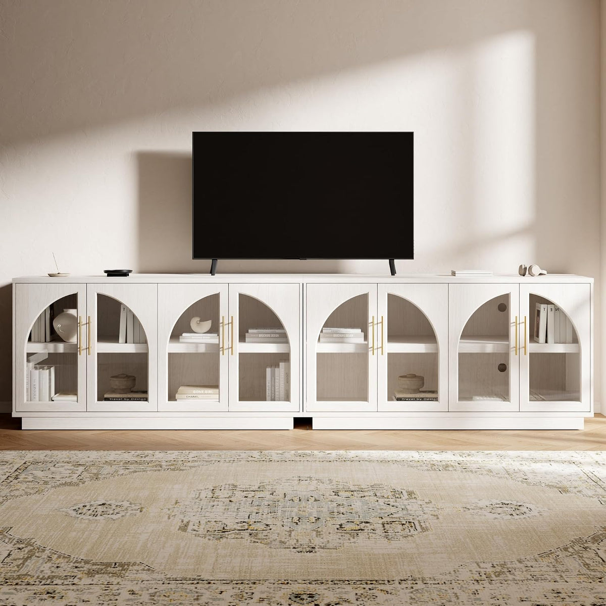 Long white oak buffet with six arched glass-front doors and gold handles topped by a TV in a neutral living room.