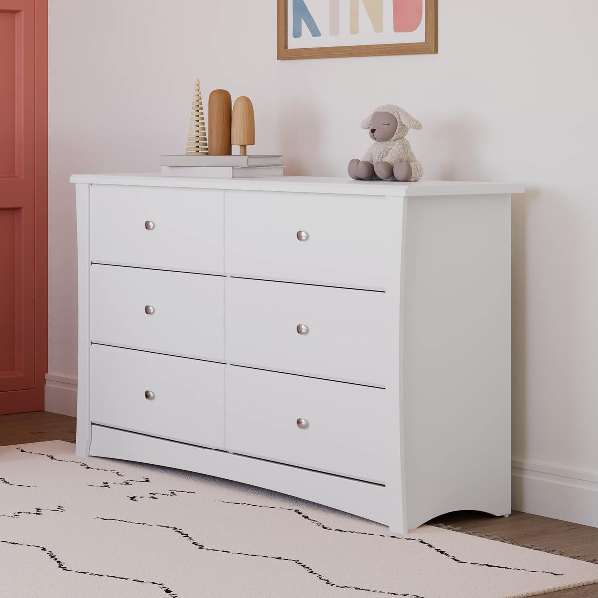 Close-up of white dresser top with stacked wooden toys and a small stuffed lamb on a nursery wall
