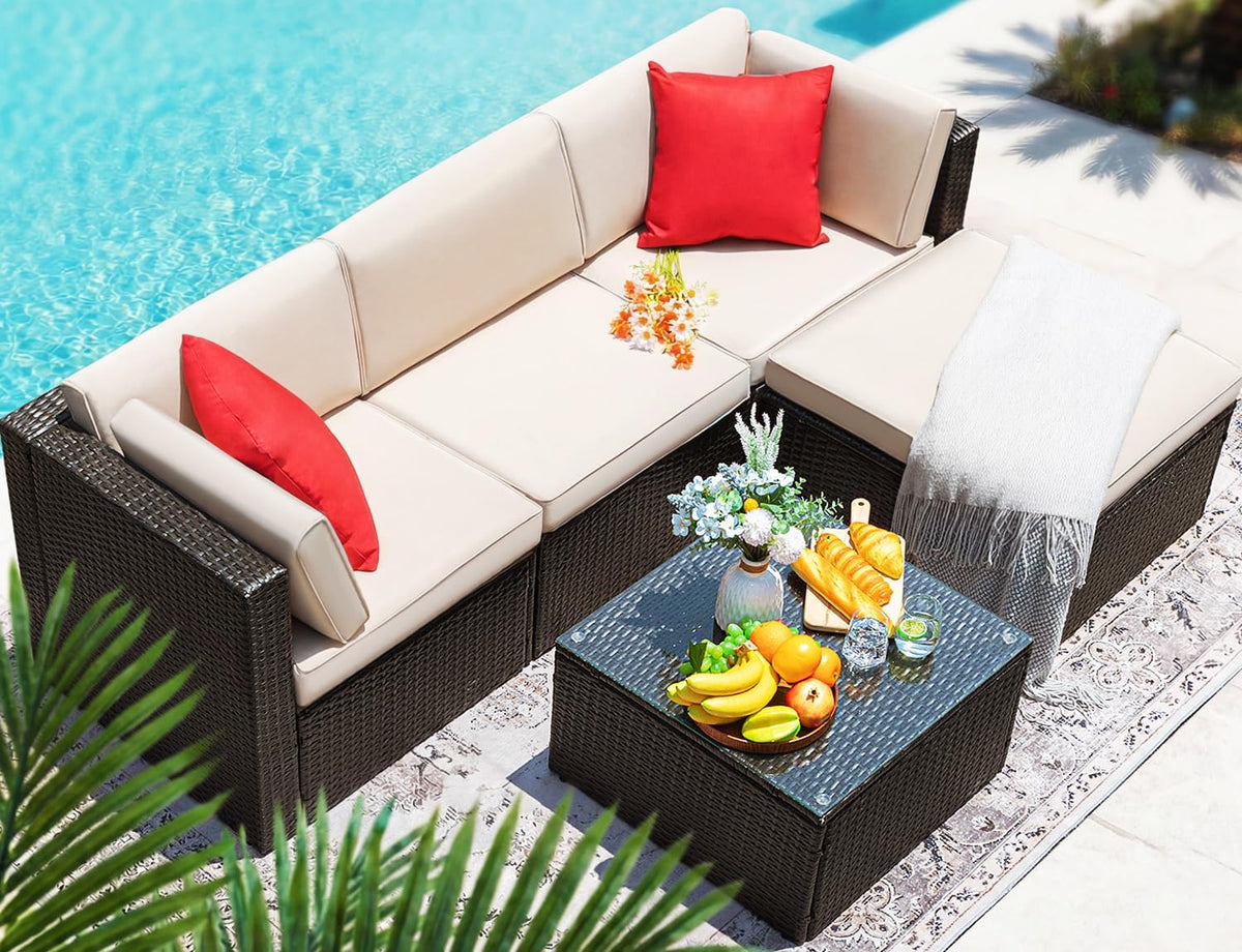 Top-down poolside view of the beige-cushioned wicker sectional with tempered-glass coffee table staged with food and decor