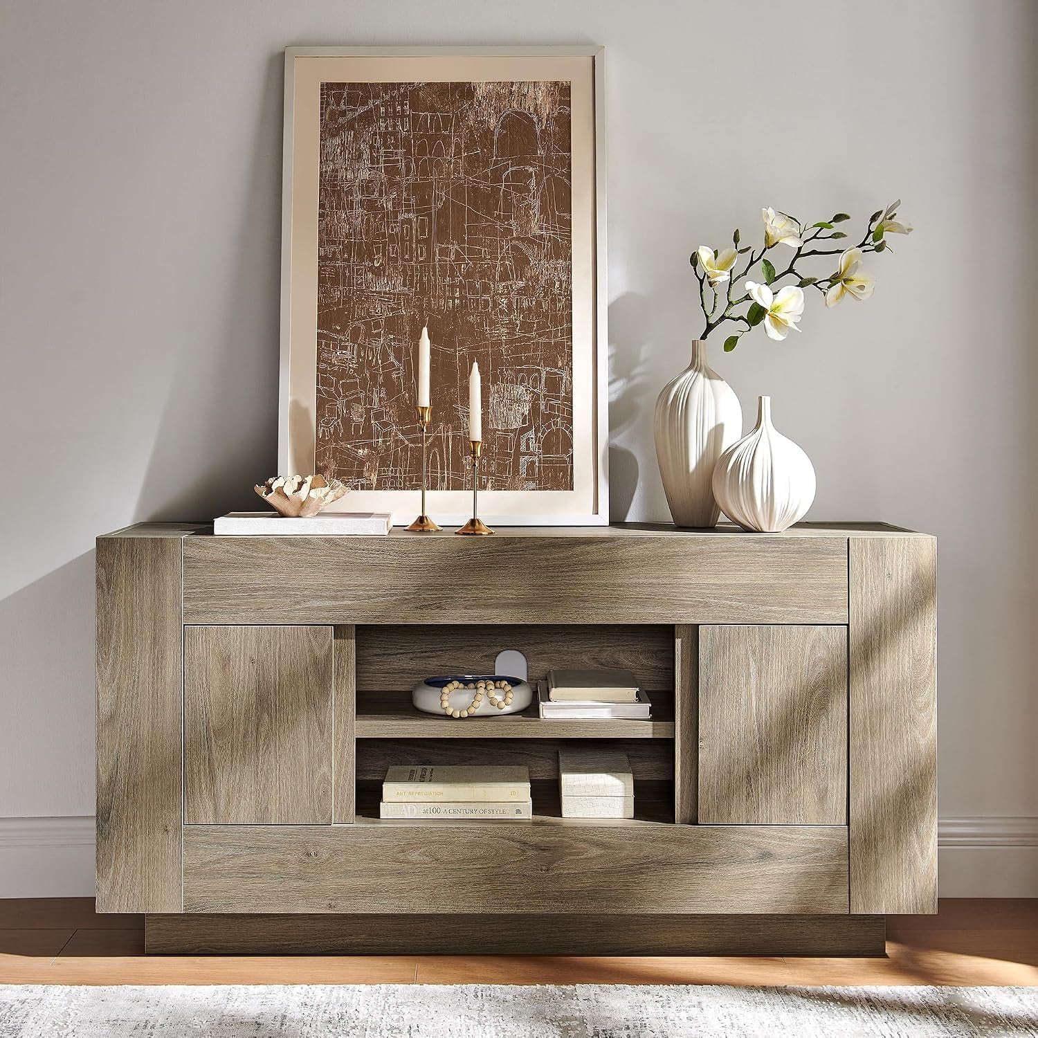 Light wood console topped with framed art, vases, and candles, center shelves holding small accessories