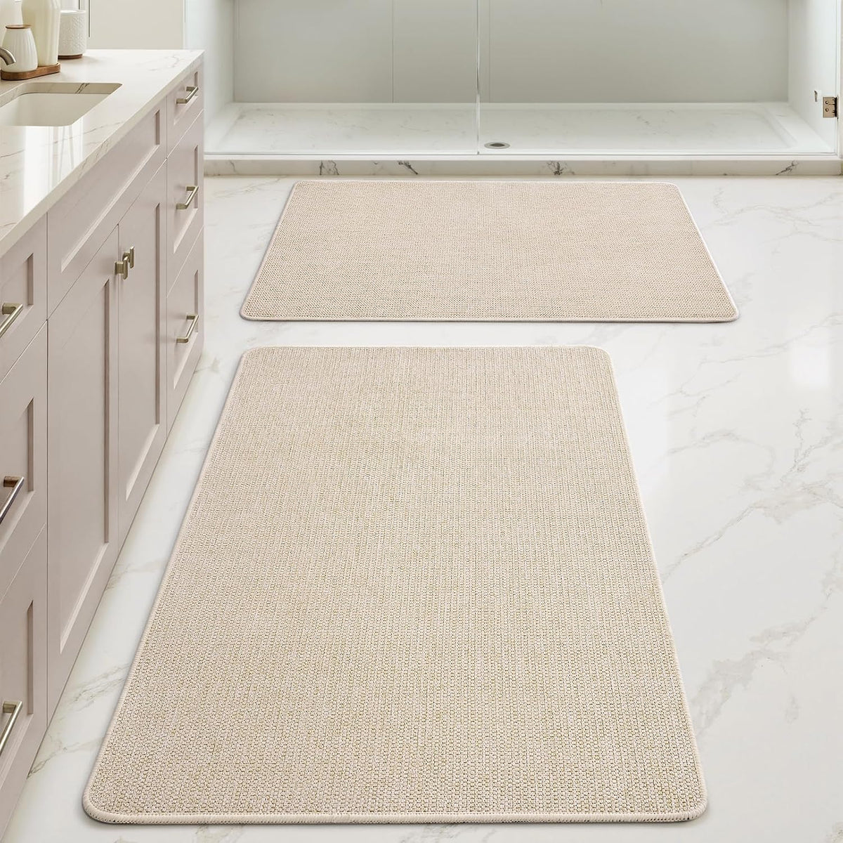 Low, close-forward perspective of a beige rectangular mat's rounded stitched edge with a second matching mat near the shower