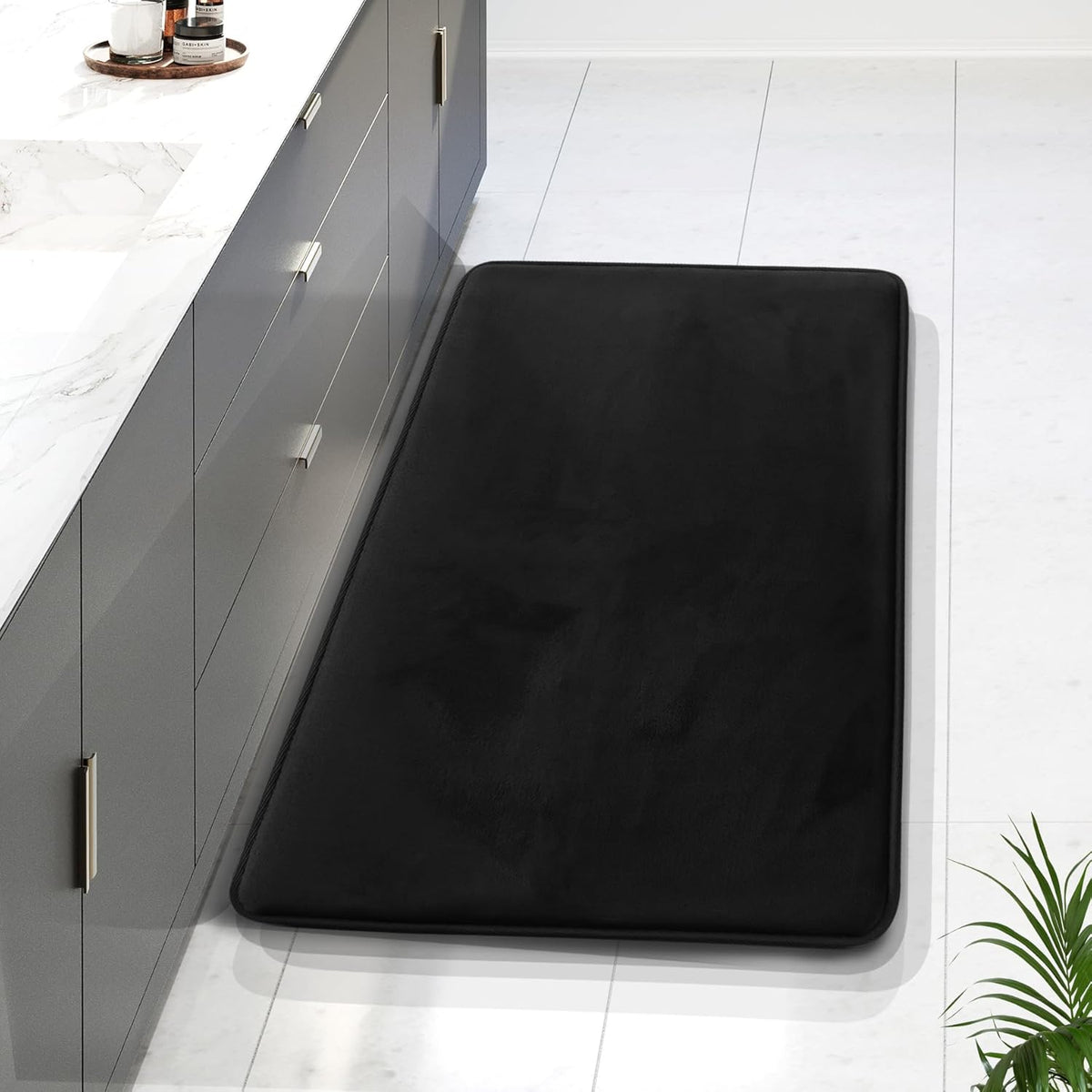Long black rectangular memory-foam rug placed along a gray vanity on white tile, photographed from above