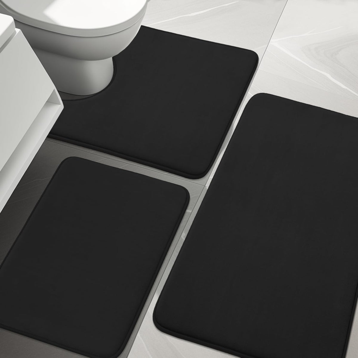 Close-up of black toilet-contour mat and rectangular bath mats on light tile floor