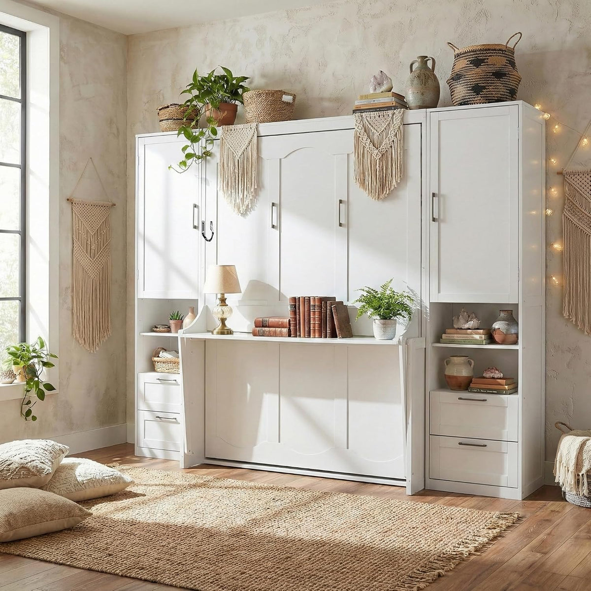 Closed white Murphy wall bed cabinet with desk folded down and decorative plants and books on top in sunlit room