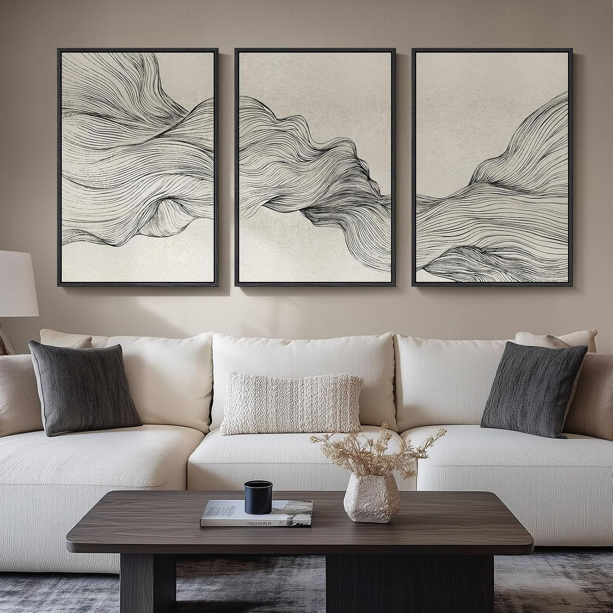 Three framed minimalist panels with flowing black line drawings on a light background above a cream sofa.