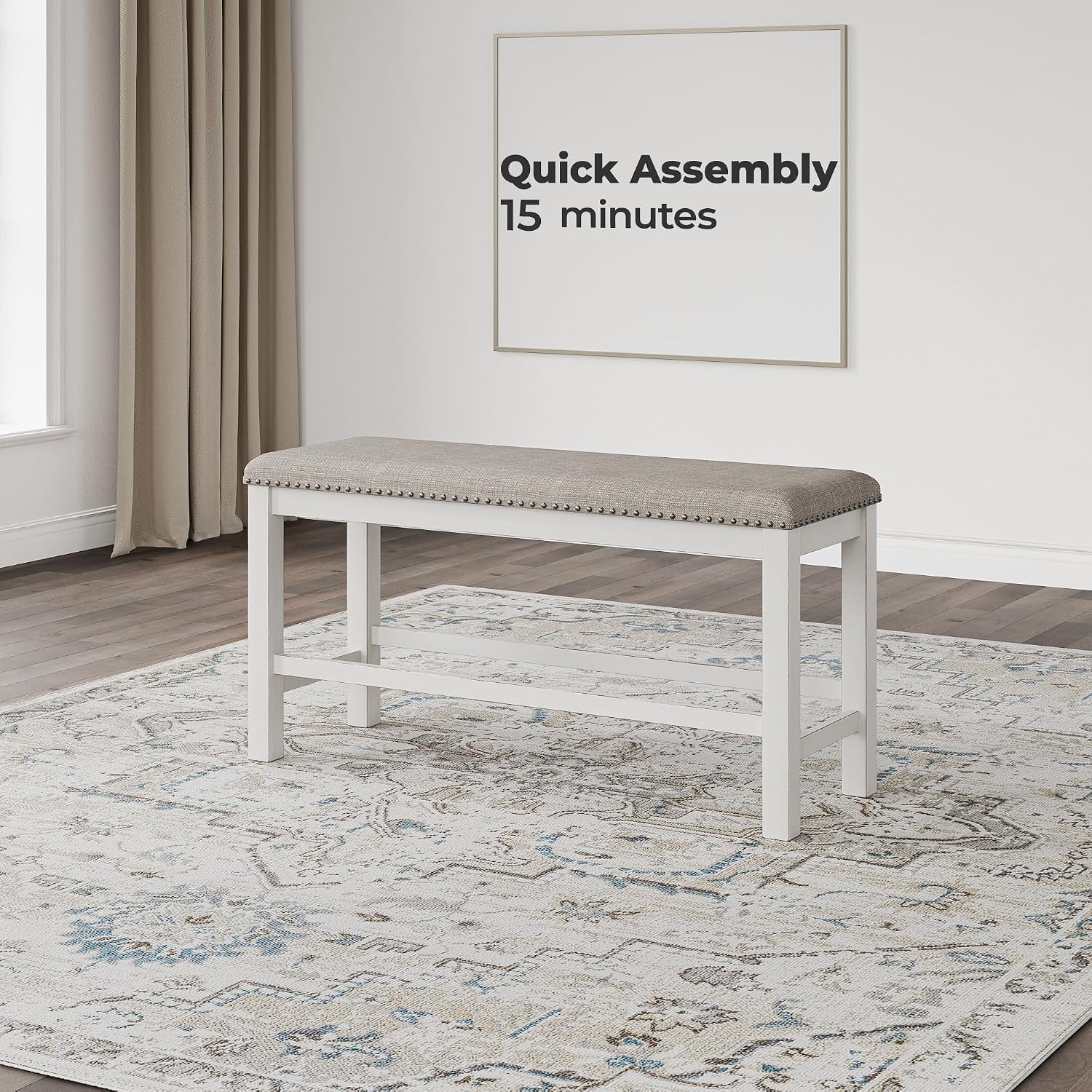 Light gray upholstered bench with antiqued white frame placed on patterned rug in a neutral living space, front view