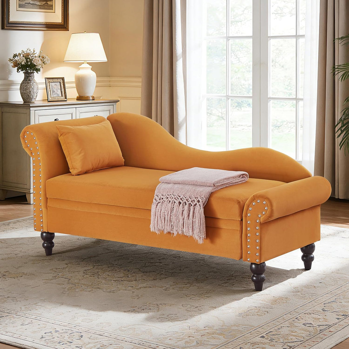 Golden-orange upholstered chaise with rolled arm, nailhead trim, and turned wooden legs in a classic living room.