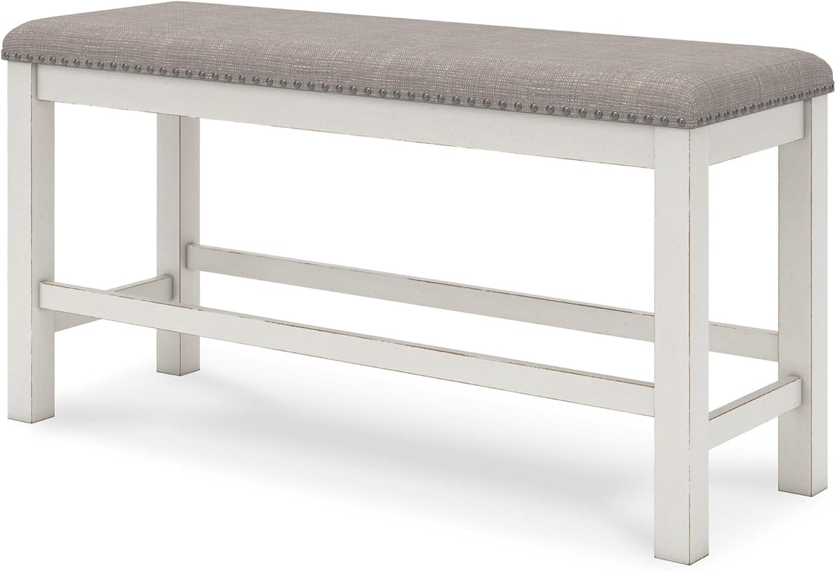 Three-quarter view of a long backless bench with a gray upholstered top and distressed white wooden base.