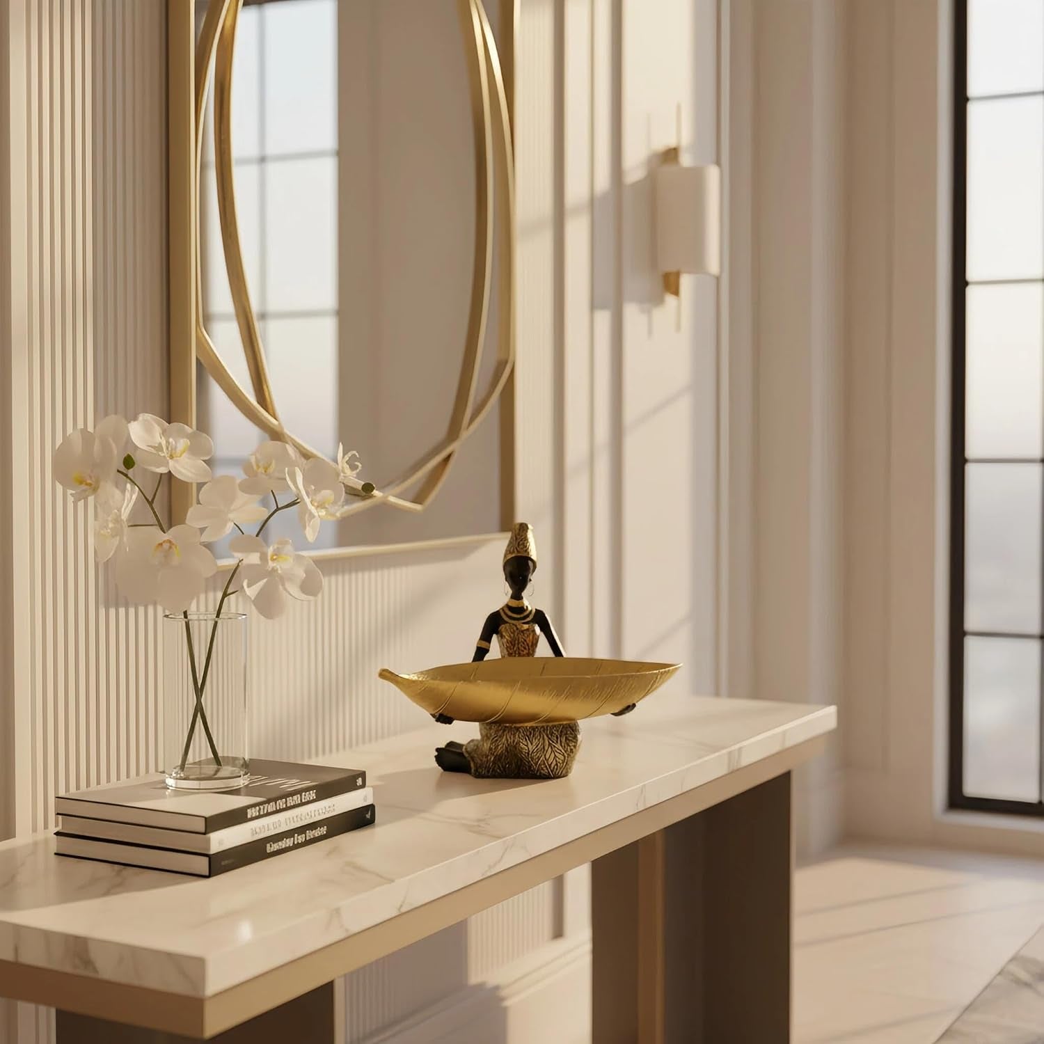 Gold leaf tray statue displayed on a light entry console beside a round mirror and a glass vase of white orchids