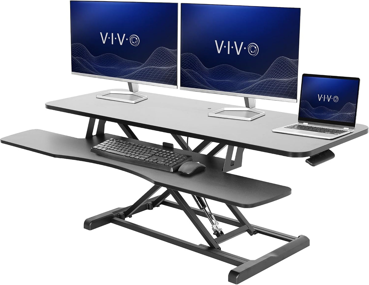 Black standing desk converter set up with dual monitors, laptop on top and keyboard and mouse on the lower shelf.