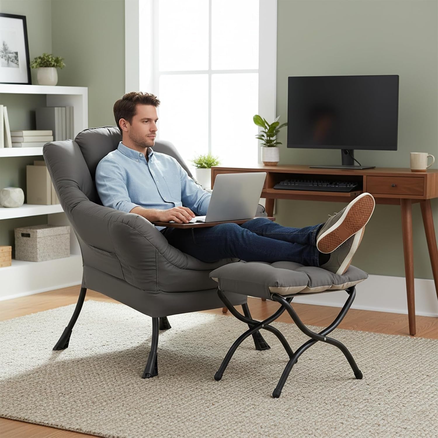 Man sitting in a dark gray lounge chair with ottoman using a laptop, feet propped on the cushioned ottoman.