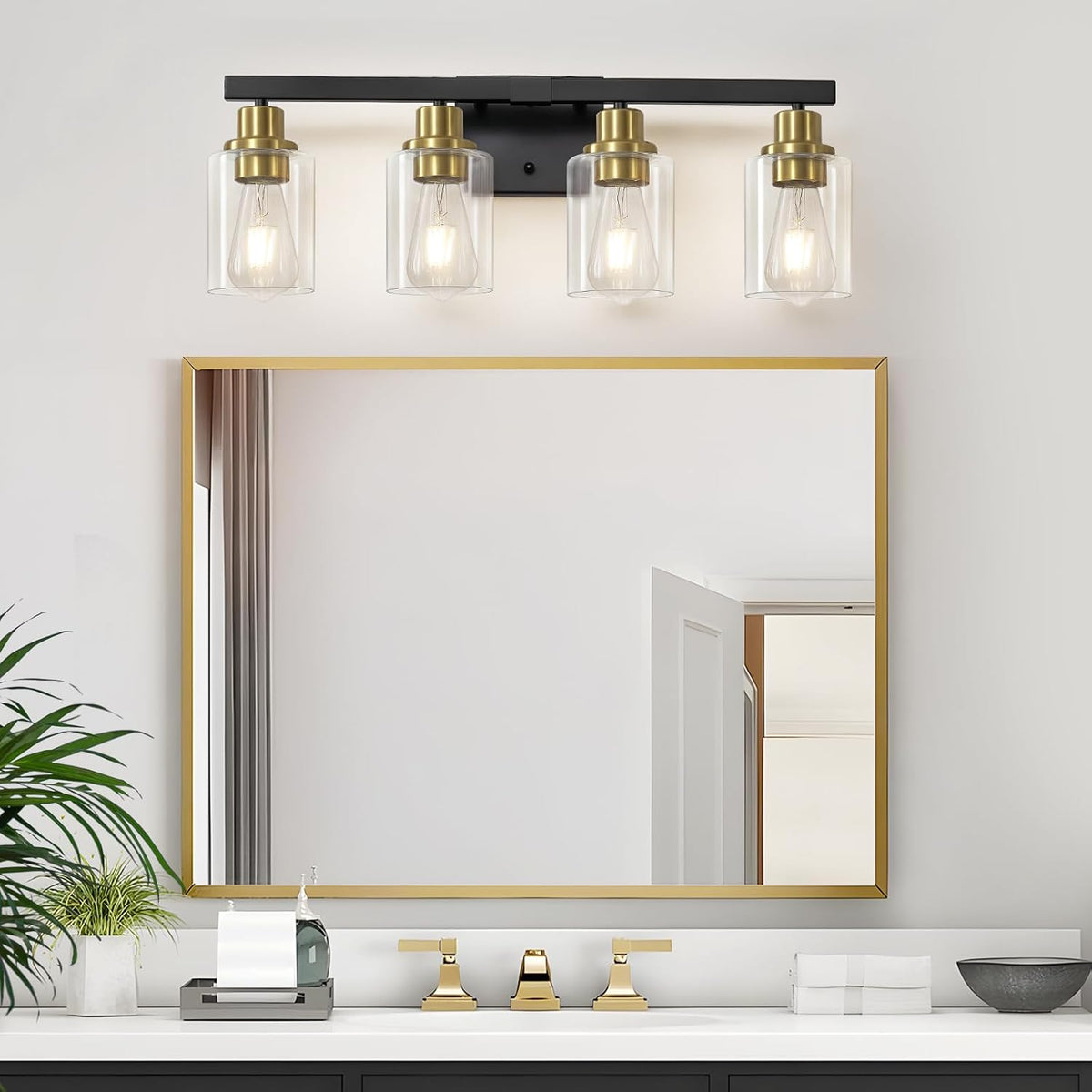 Four-light vanity fixture mounted above a gold-framed mirror in a bathroom, with sink and gold faucet visible below.