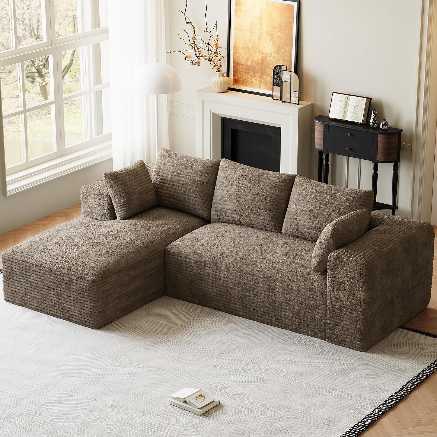 Three-quarter angled view of a brown corduroy L-shaped sectional with chaise on the left near a window and fireplace.