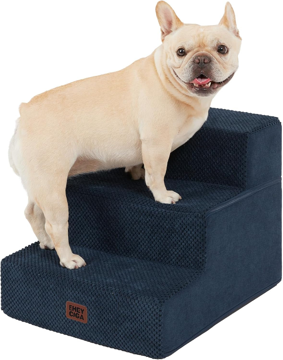 Front-close view of a cream French bulldog perched on navy blue textured foam stairs, facing the camera.