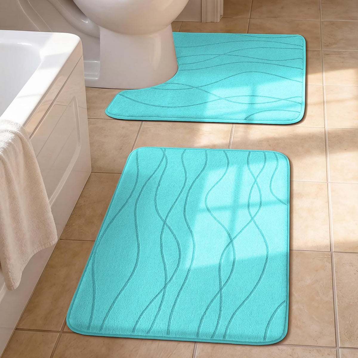 Two turquoise bath mats on a tiled floor by a bathtub and a toilet, sunlight casting window shadows.