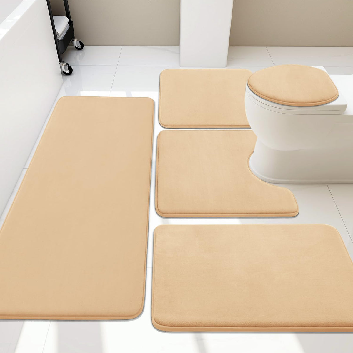 Beige memory-foam bath rugs arranged around a white toilet on light tile flooring