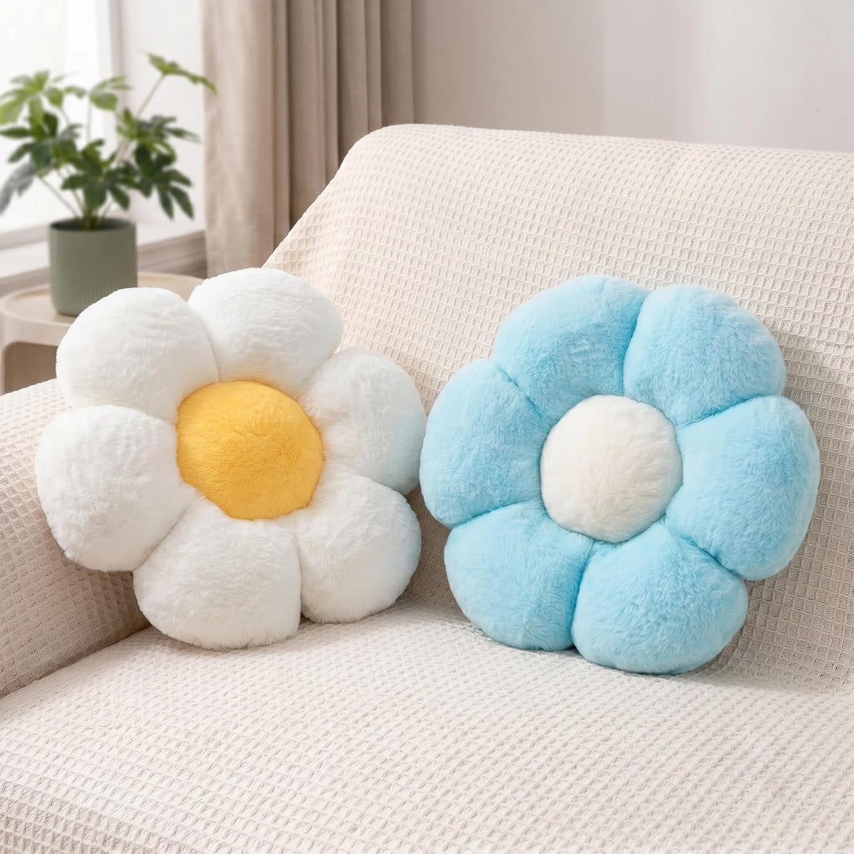 Pair of plush daisy pillows on a sofa — one white with yellow center, one light blue with cream center.