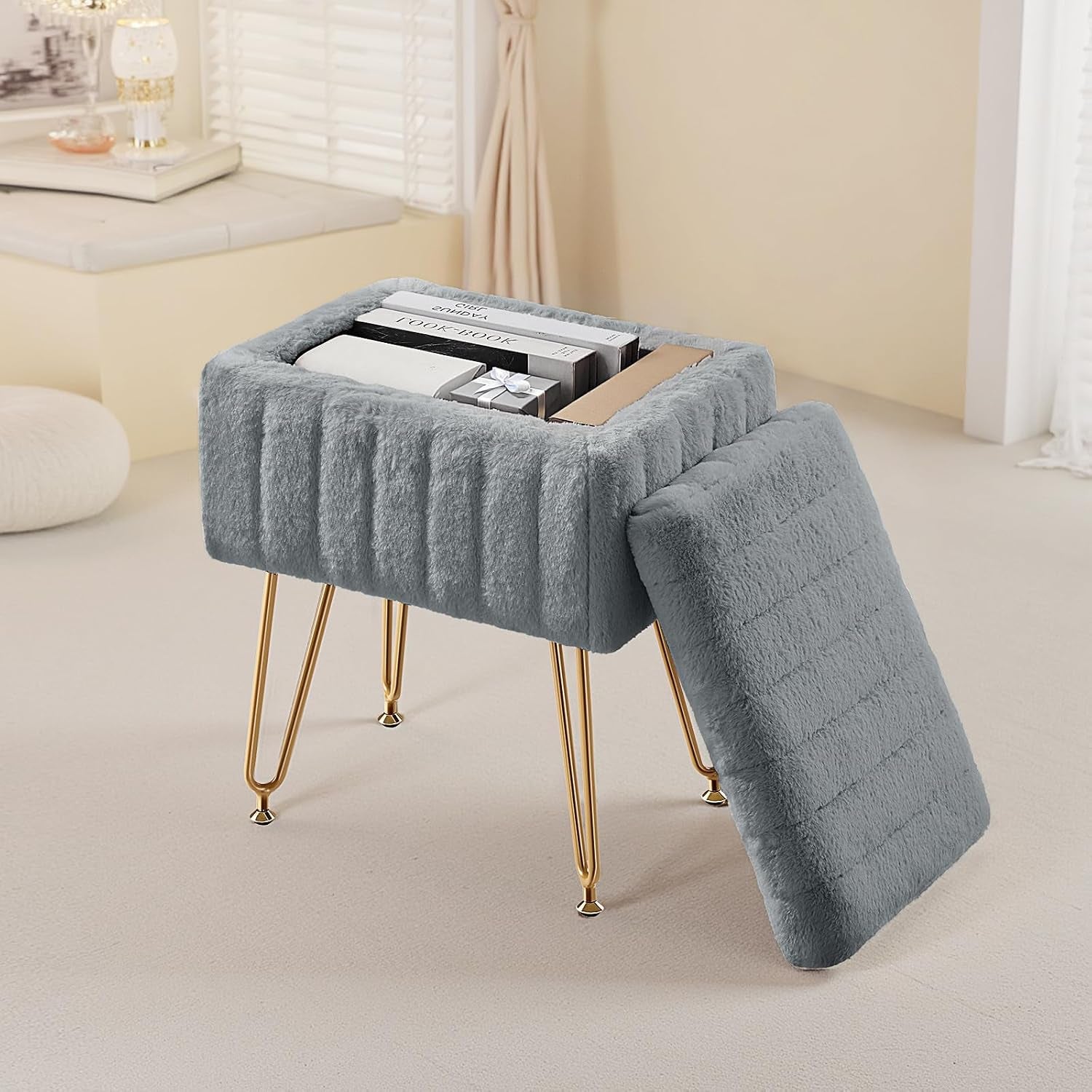 Gray faux-fur vanity stool with gold legs, lid removed and leaning, interior holding books and boxes