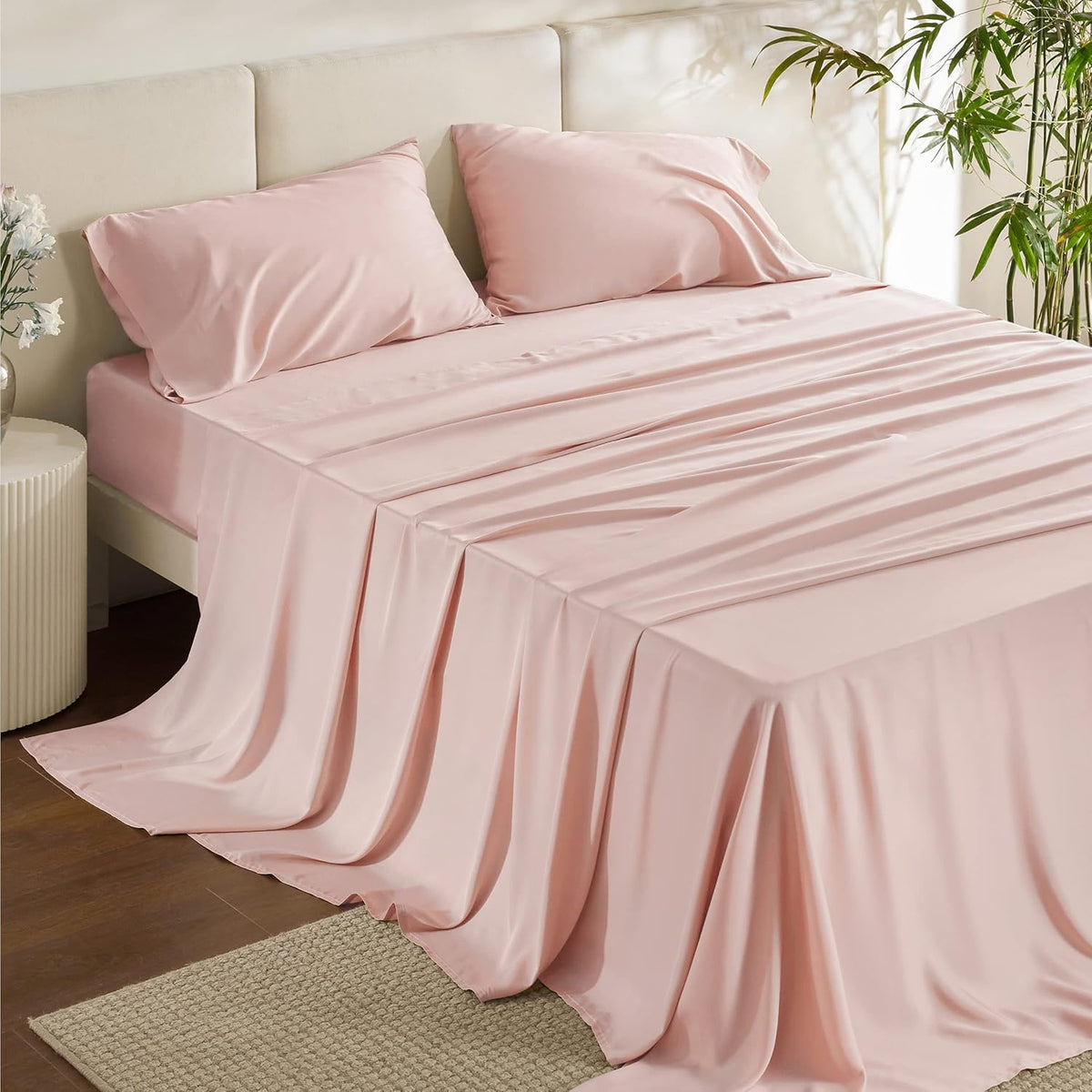 Queen bed with blush-pink silky sheets and two matching pillows draped to the floor