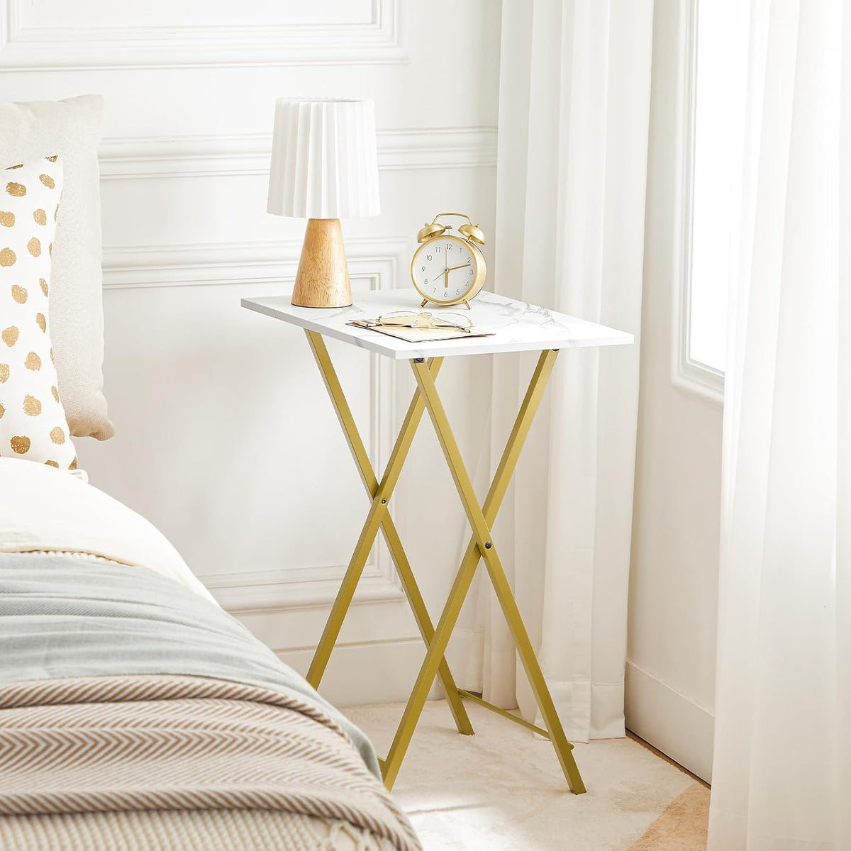 Marble-pattern folding side table with gold metal X-frame used as a bedside table with a lamp and alarm clock