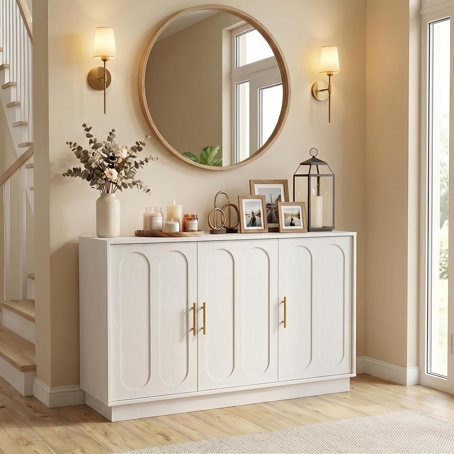 White fluted credenza beneath a large round mirror, decorated with candles, photos and wall sconces.