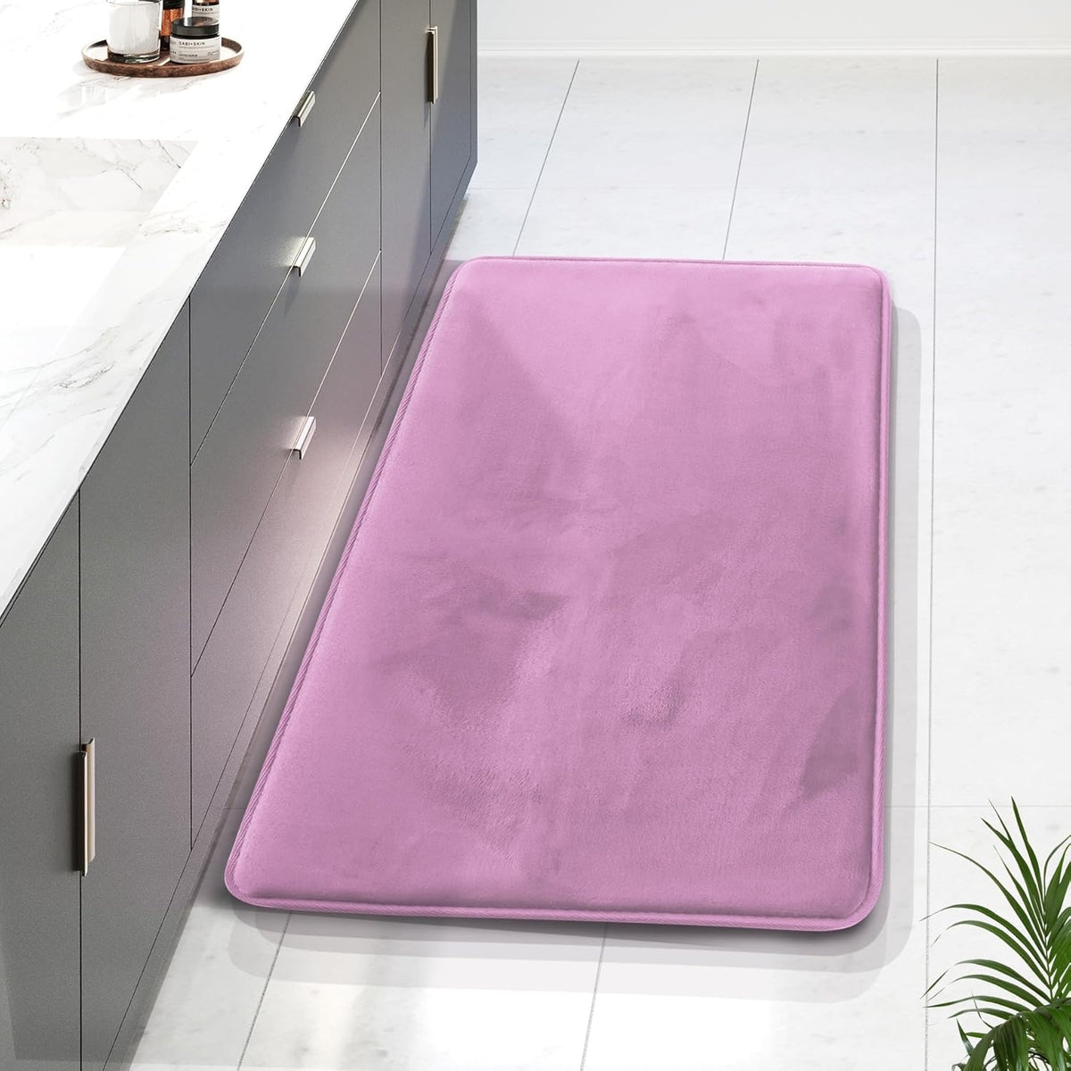 Top-down view of a long pink memory-foam runner placed beside a gray bathroom vanity on light tile.